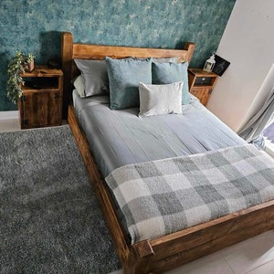 May include: A wooden bed frame with a grey and white checked blanket and grey pillows. The bed is in a room with a teal textured wall and a wooden bedside table on each side.