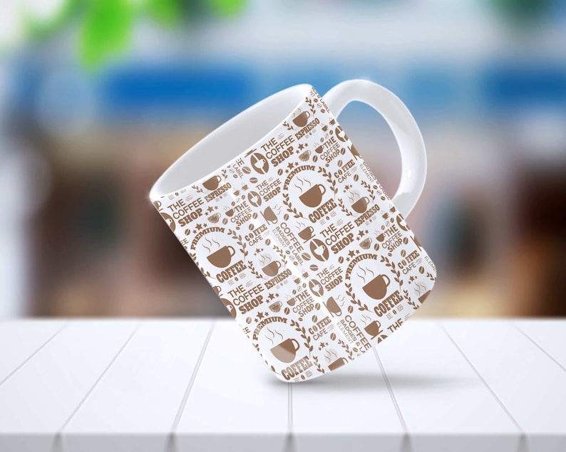 May include: White ceramic coffee mug with a brown and white pattern. The pattern features the text "The Coffee Shop" and coffee bean illustrations.