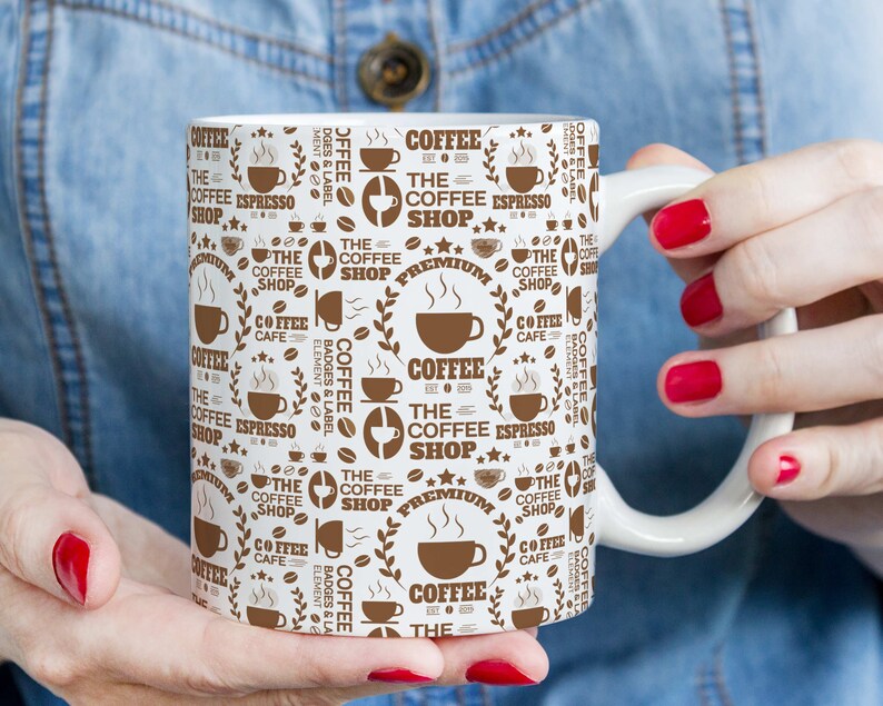 May include: White ceramic coffee mug with a brown and white design featuring the text "The Coffee Shop" and other coffee-related words and graphics.