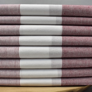 May include: A stack of six rectangular towels. Each towel has a white center section and burgundy striped ends. The towels are folded and stacked, with the fringed edges of the top towel visible. The towels are made of a woven fabric.