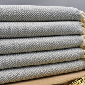May include: A stack of five gray and white patterned Turkish towels with fringe. The towels are folded and stacked on a wooden surface.