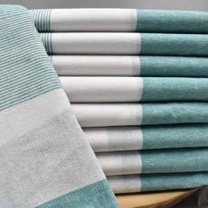 May include: A stack of white and teal striped kitchen towels with fringed edges. The towels are folded and stacked on top of each other.