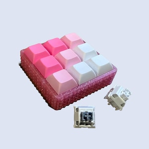 May include: A set of 9 pink and white keycaps in a pink plastic case. Two additional keycaps are shown separately.