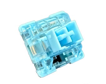 May include: A clear blue mechanical keyboard switch with a light blue stem. The switch is designed for a tactile typing experience.