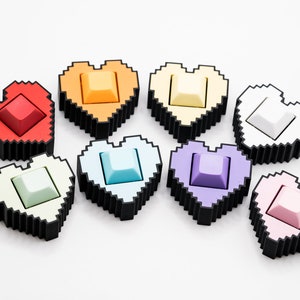 May include: Eight pixel heart-shaped keycaps in different colors: red, orange, yellow, white, light blue, purple, green, and pink.