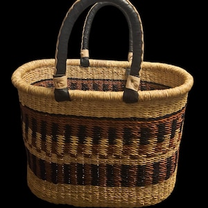 May include: Woven basket with a rounded shape and two arched handles. The basket features a natural tan colour with horizontal bands of brown and black geometric patterns. The handles are black with tan leather accents.