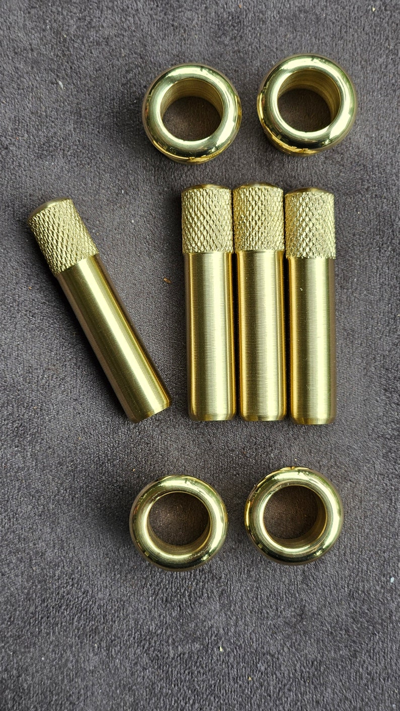 Puede incluir: Un juego de ojales y arandelas de metal de color dorado. Los ojales son redondos con un agujero en el centro. Las arandelas son cil&iacute;ndricas con una parte superior moleteada.