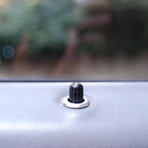 May include: A close-up of a black door handle with a silver ring around it. The handle is on a gray car door.