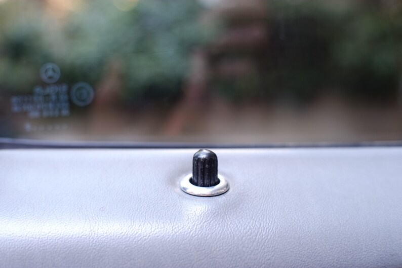 May include: A close-up of a black door handle with a silver ring around it. The handle is on a gray car door.