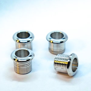 May include: Four silver metal guitar strap button grommets. The grommets are cylindrical with a raised lip around the top edge. The grommets are designed to be used with a guitar strap.