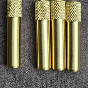 Puede incluir: Cuatro pomos de metal de color dorado con un patr&oacute;n de diamante en la parte superior. Los pomos est&aacute;n dispuestos en una fila sobre una superficie gris texturizada.