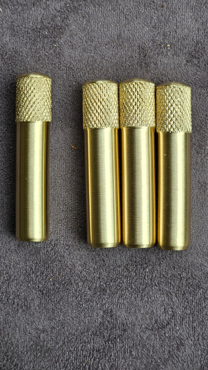 Puede incluir: Cuatro pomos de metal de color dorado con un patr&oacute;n de diamante en la parte superior. Los pomos est&aacute;n dispuestos en una fila sobre una superficie gris texturizada.