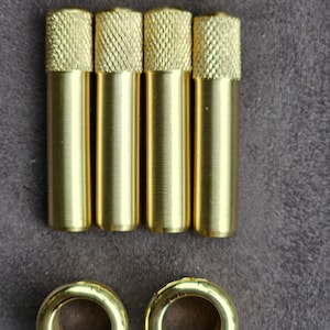 Puede incluir: Conjunto de seis ojales de metal dorado y cuatro varillas de metal dorado. Los ojales son redondos con un agujero en el centro. Las varillas son cil&iacute;ndricas con una superficie texturizada.