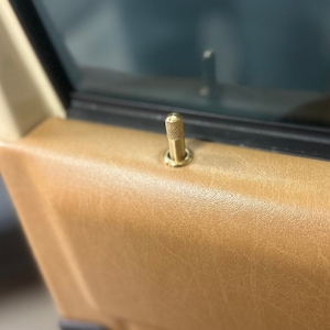 Puede incluir: Primer plano de una manija de puerta de lat&oacute;n con un pomo moleteado. La manija est&aacute; montada en un panel de puerta de cuero marr&oacute;n.