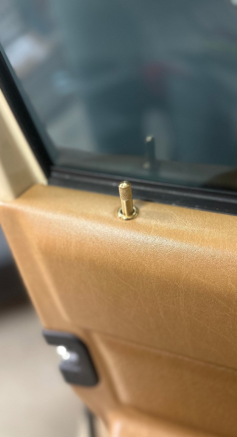 Puede incluir: Primer plano de una manija de puerta de lat&oacute;n con un pomo moleteado. La manija est&aacute; montada en un panel de puerta de cuero marr&oacute;n.