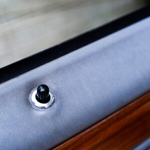 May include: Close-up of a black door handle with a silver trim on a gray car door panel.