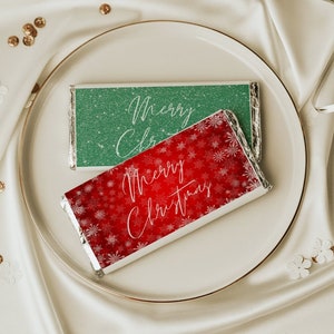 May include: Two Christmas-themed chocolate bar wrappers. One is green with glitter and says "Merry Christmas". The other is red with snowflakes and says "Merry Christmas".