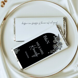 May include: Two white chocolate bars with silver foil wrapping, displayed on a white plate. One bar has the text "Thank you for coming to celebrate our wedding." The other bar has the text "B&N MR & MRS Kennedy 20.02.2025" with floral accents.