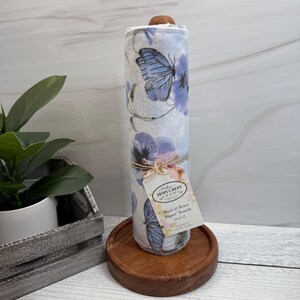 May include: A roll of Wash & Reuse "Paper" Towels, featuring a butterfly and floral design in shades of blue and white. The towels are tied with twine and a tag. The roll is displayed on a wooden stand.
