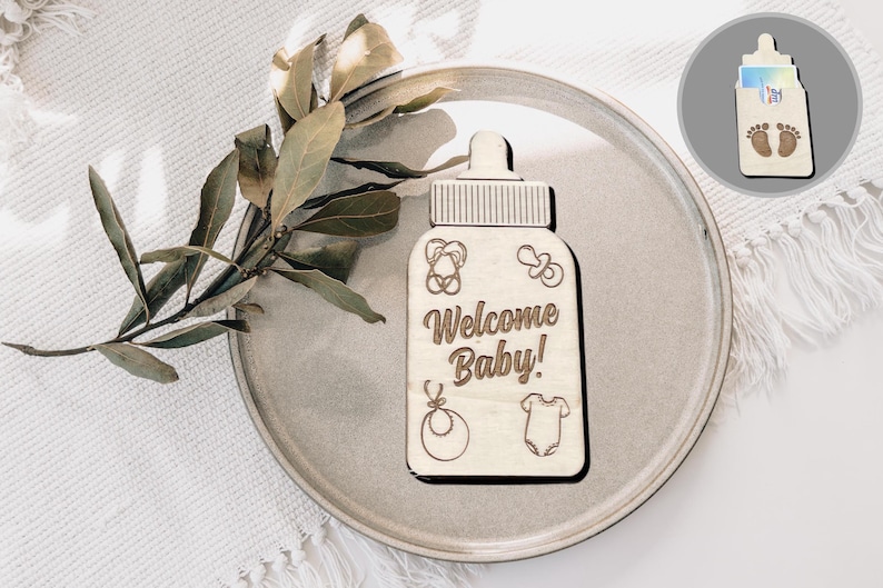 Könnte beinhalten: Ein hölzernes Willkommens-Schild in Form einer Babyflasche mit dem Text "Willkommen Baby!" und kleinen gravierten Bildern von einem Schnuller, einer Rassel und einem Strampler.