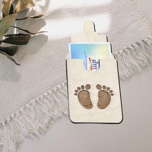 May include: Wooden baby bottle shaped card holder with a white card inside. The card holder has a cutout of two baby footprints.