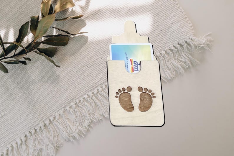 May include: Wooden baby bottle shaped card holder with a white card inside. The card holder has a cutout of two baby footprints.