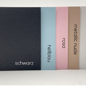May include: Six cardstock paper samples in different colors, including black, light blue, pink, nude, pearl white, and metallic silver. The colors are labeled in German.