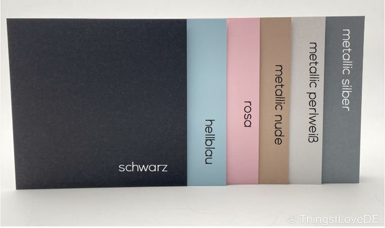 May include: Six cardstock paper samples in different colors, including black, light blue, pink, nude, pearl white, and metallic silver. The colors are labeled in German.