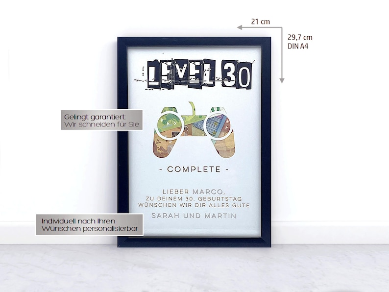Op de afbeelding: Een zwart ingelijste poster met een witte achtergrond. De poster heeft een zwart-witte afbeelding van een videogamecontroller met de tekst "LEVEL 30" erboven. De tekst "COMPLETE" staat onder de controller. De poster bevat ook de tekst "Lieber Marco, zu deinem 30. Geburtstag w&uuml;nschen wir dir alles gute Sarah und Martin".