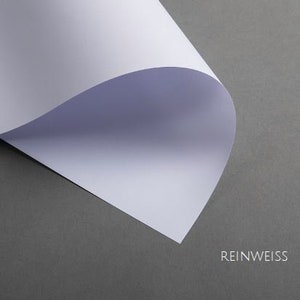 May include: A close-up of a white sheet of paper folded in half, with the text "REINWEISS" printed in black at the bottom.