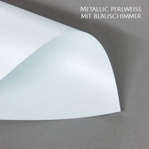 May include: A sheet of metallic pearl white paper with a blue shimmer. The paper is folded in half and the top half is lifted up to show the shimmer.