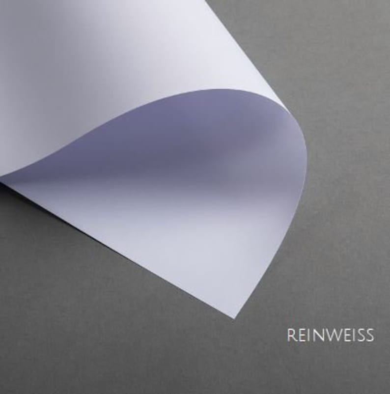 May include: A close-up of a white sheet of paper folded in half, with the text "REINWEISS" printed in black at the bottom.