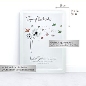 May include: A white frame with a white mat and a printed image of a dandelion with colorful birds flying away. The text "Zum Abschied..." is at the top of the image. The text "Vielen Dank f&uuml;r die gute Zeit. wir werden Dich vermissen! Sarah & Martin" is at the bottom of the image. The text "Individuell nach Ihren W&uuml;nschen personalisierbar" is at the bottom of the frame. The frame is 21 cm by 29.7 cm.