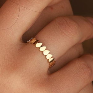 Op de afbeelding: Een gouden ring met een traanvormig ontwerp. De ring is gemaakt van een dunne band en heeft een rij traanvormige stenen.