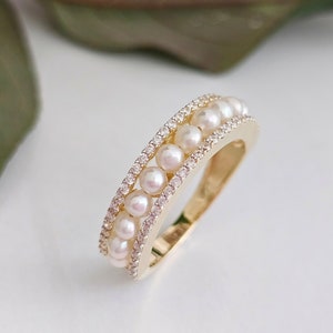 Puede incluir: Un anillo de oro con una doble fila de perlas blancas. El anillo está sobre un fondo blanco.