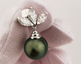 Könnte beinhalten: Ein schwarzer Perlenohrring mit einem Diamantenblumenmuster. Die Perle ist dunkelgrün und die Diamanten sind klar.
