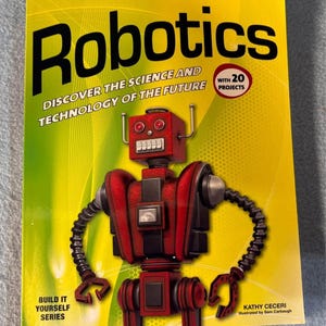 May include: A book titled "Robotics" with a red robot illustration on the cover. The book's title is in large black letters, with the subtitle "Discover the Science and Technology of the Future." It also states "With 20 Projects."