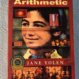 May include: A hardcover book titled "The Devil's Arithmetic" by Jane Yolen. The cover features a portrait of a young person, with illustrations of a chalice, a Star of David, and other images. The book has a National Jewish Book Award seal.