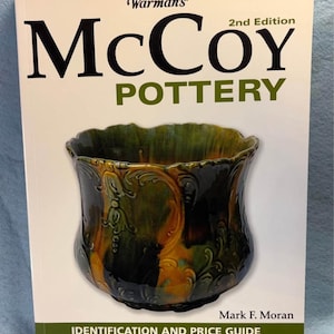 May include: A book titled "Warman's McCoy Pottery 2nd Edition" with a green and brown pottery piece on the cover. The book is a guide for identification and price. The author is Mark F. Moran.