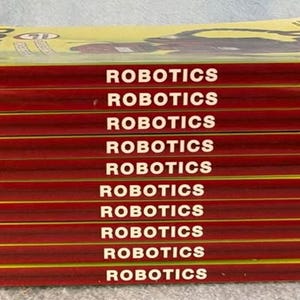 May include: A stack of ten books titled "ROBOTICS" with red and yellow covers. The author's name, CECERI, is printed on the side of each book. The publisher's name, nomad press, is printed on the side of each book.