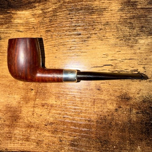 May include: A tobacco pipe featuring a polished dark brown wooden bowl, a smooth black stem, and a silver-colored metal band connecting the two sections. The pipe has a classic curved shape with a cylindrical bowl and a tapered mouthpiece.