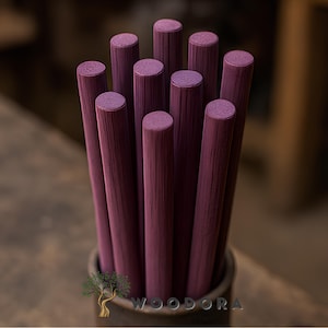 May include: A bundle of ten cylindrical wooden dowels, each painted a deep burgundy color. The dowels are arranged vertically in a dark container, with the tops of the dowels visible. The wood grain is visible on the dowels. The logo "WOODORA" is visible.