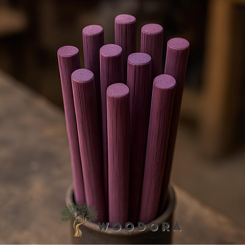 May include: A bundle of ten cylindrical wooden dowels, each painted a deep burgundy color. The dowels are arranged vertically in a dark container, with the tops of the dowels visible. The wood grain is visible on the dowels. The logo "WOODORA" is visible.