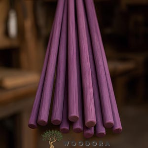 May include: A bundle of purple wooden dowels, each with a rounded end. The dowels are arranged together, showcasing their uniform color and texture. The background is blurred, highlighting the dowels.