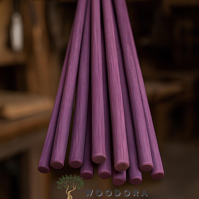 May include: A bundle of purple wooden dowels, each with a rounded end. The dowels are arranged together, showcasing their uniform color and texture. The background is blurred, highlighting the dowels.