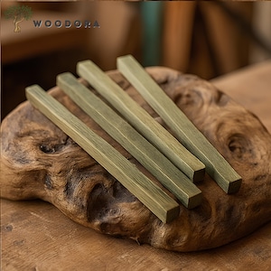 May include: Five wooden sticks with a green stain finish, arranged on a wooden surface. The sticks are all the same length and width, and they are all aligned in the same direction. The sticks are made of a light-colored wood, and they have a smooth, polished finish.