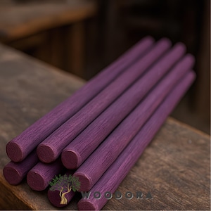 May include: A close-up shot displays several cylindrical wooden dowels, each approximately 12 inches long, dyed a deep purple hue. The wood grain is visible, adding texture. The dowels are arranged on a wooden surface, suggesting a craft or woodworking theme.