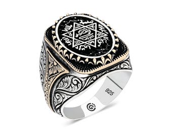 May include: A silver ring with a black and gold design. The ring features a central black oval with a white star and Arabic script. The band has ornate floral patterns and the hallmark "925".
