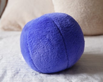 May include: A soft, round, blue plush pillow on a white linen bedspread.