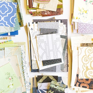 May include: A collection of patterned scrapbook paper in various colors and designs, including floral, geometric, and abstract patterns. The paper is arranged in stacks and piles, with some pieces overlapping.